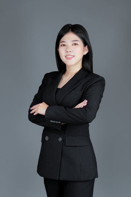 Studio shot of a woman in a black suit posing confidently against a gray background.