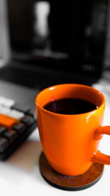 A vibrant orange coffee mug filled with coffee on a modern workspace desk.