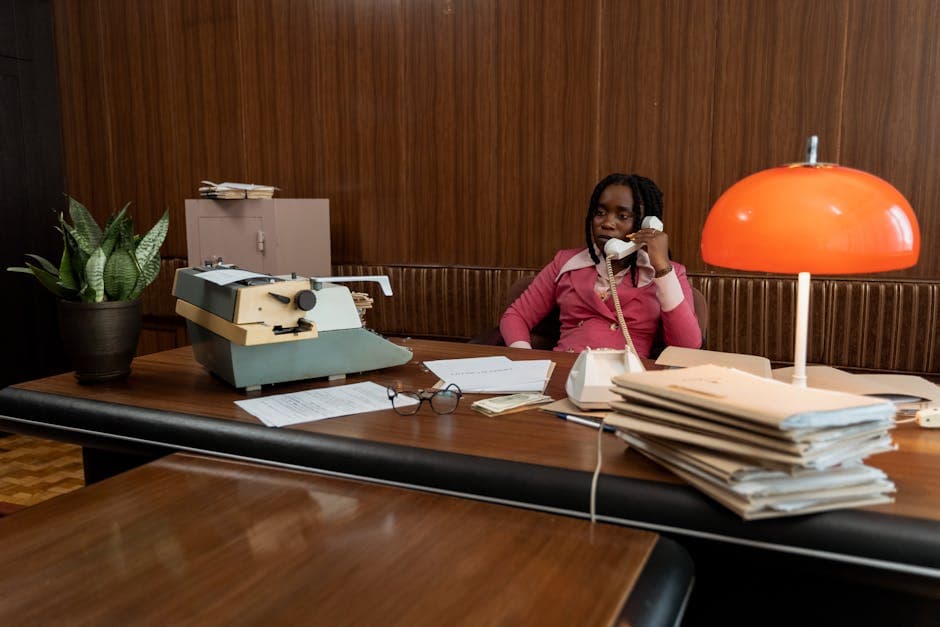 A woman in a retro office setting making a phone call with vintage decor and a typewriter.