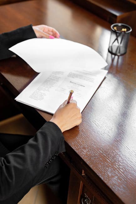 Close-up of a business professional signing a paper document at a wooden desk.