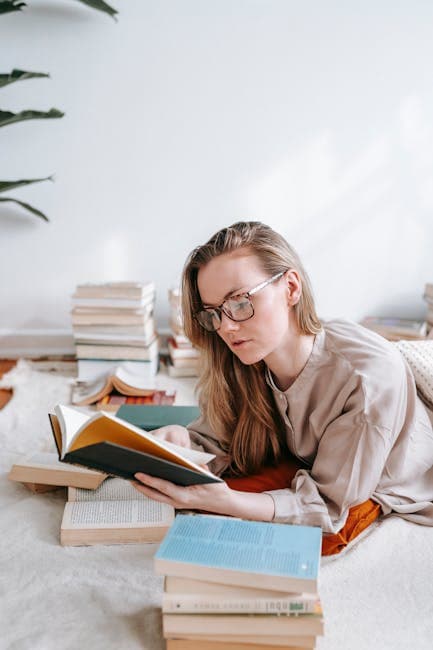 Side view of female with long hair in eyeglasses reading book attentively while lying on plaid