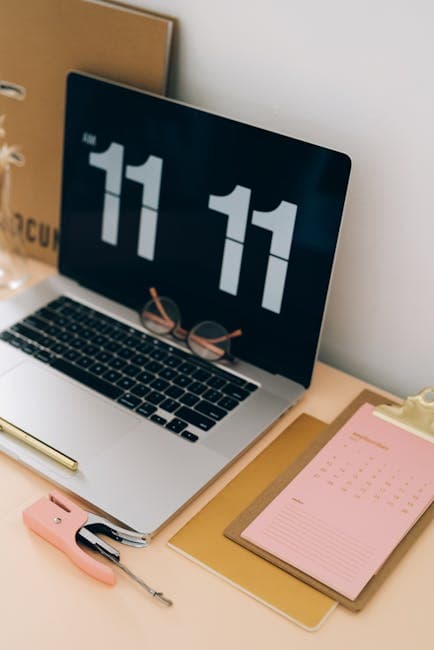 Stylish workspace featuring a laptop showing time, clipboard with a calendar, and glasses.
