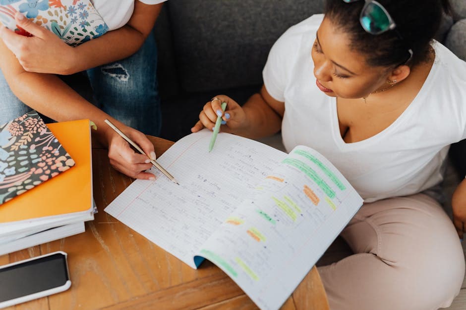Two adults collaborate on educational content with notebooks and pens indoors.