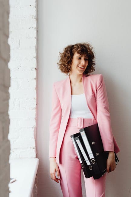 Smiling woman in a pink suit holding binders, embodying modern business chic.
