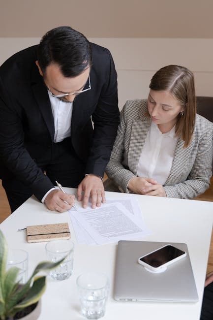 Two business professionals signing a contract at a desk; collaborating in an office.