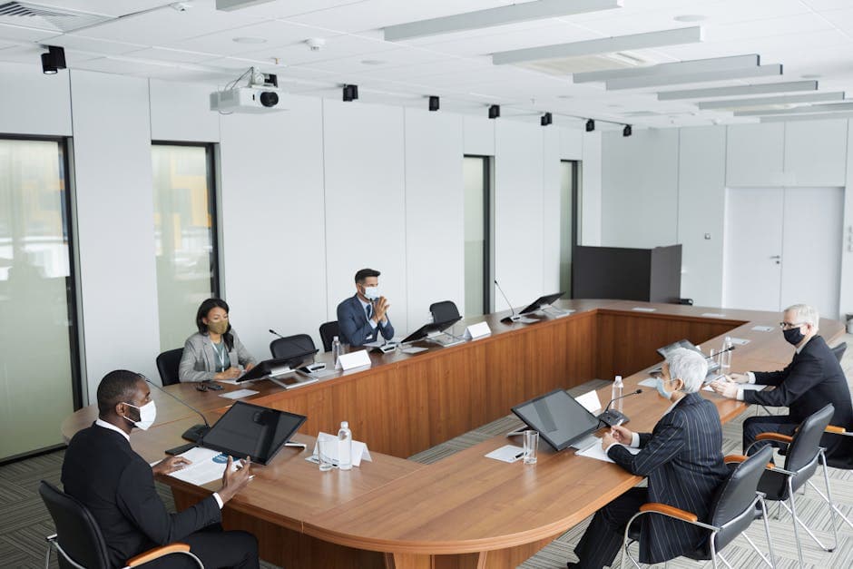 Business professionals wearing masks attending a conference meeting in a modern setting.