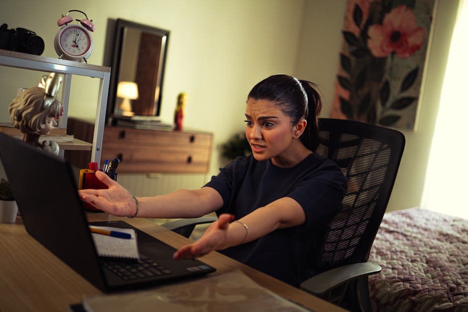 A woman appears frustrated while working on her laptop in a well-decorated home office.