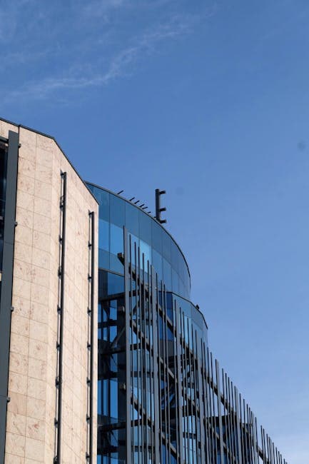 Sharp architectural contrast of glass and stone facade on a modern office building under clear blue skies.