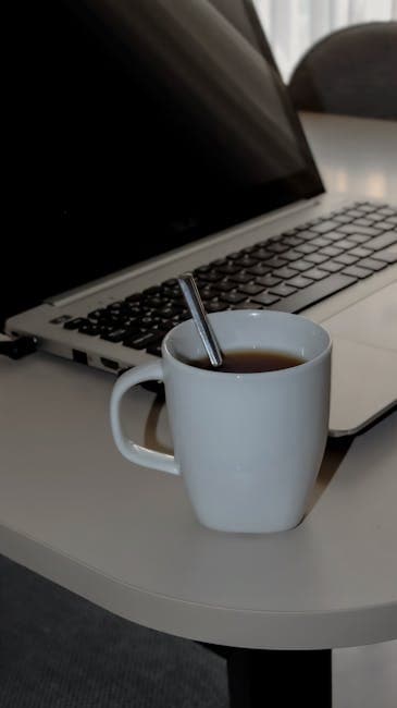 A cozy workspace setup featuring a white coffee mug with a spoon beside an open laptop on a desk.