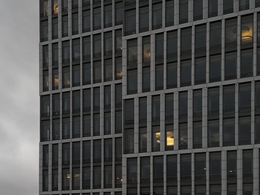 Close-up of a modern office building facade with glowing lights seen through windows at dusk.