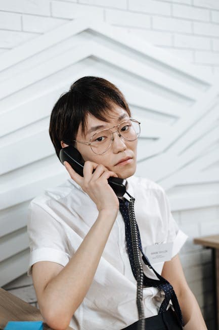 Portrait of an Asian man with eyeglasses talking on a phone in a call center.