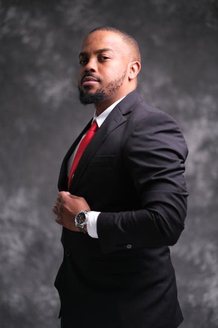 Portrait of a confident man wearing a black suit and red tie, looking assertive.