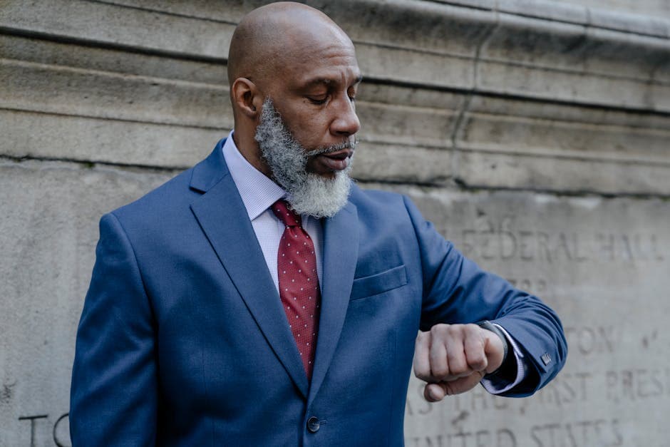 African American businessman checking watch, standing against stone wall.