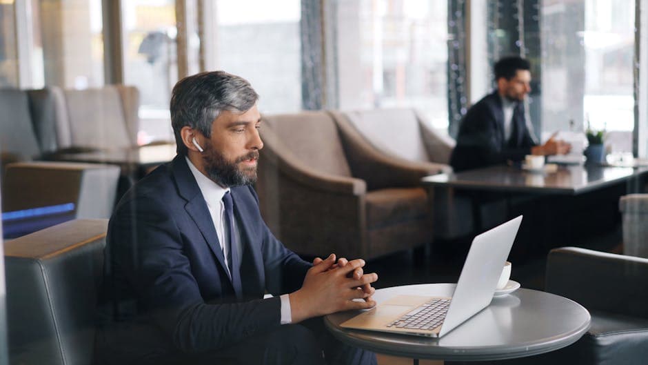 Professional businessman in a café using a laptop and earphones for a video call.