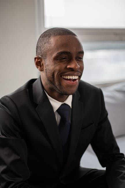 Portrait of a happy businessman in a black suit, smiling with confidence in an indoor setting.