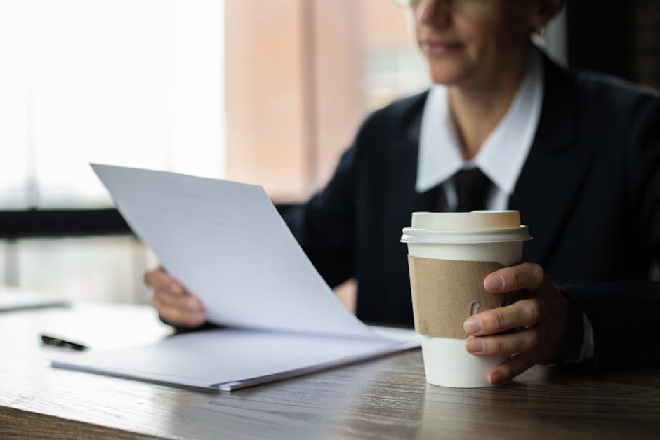 Focused businesswoman examining documents with a disposable coffee cup on a wooden desk.