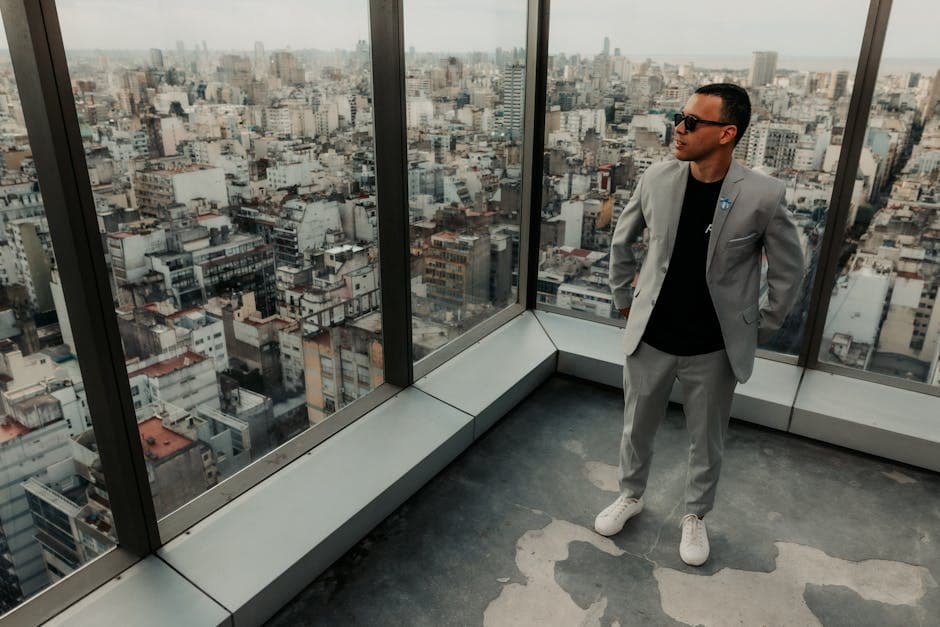 Man in gray suit with sunglasses on a skyscraper, gazing over Buenos Aires cityscape.