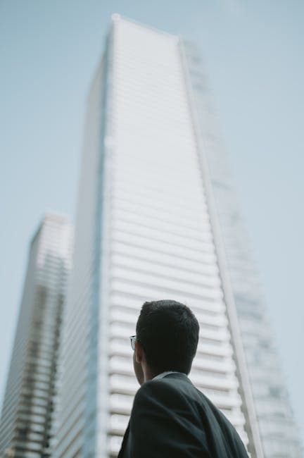Man in glasses observing tall modern skyscrapers, showcasing contemporary architecture from a low angle.