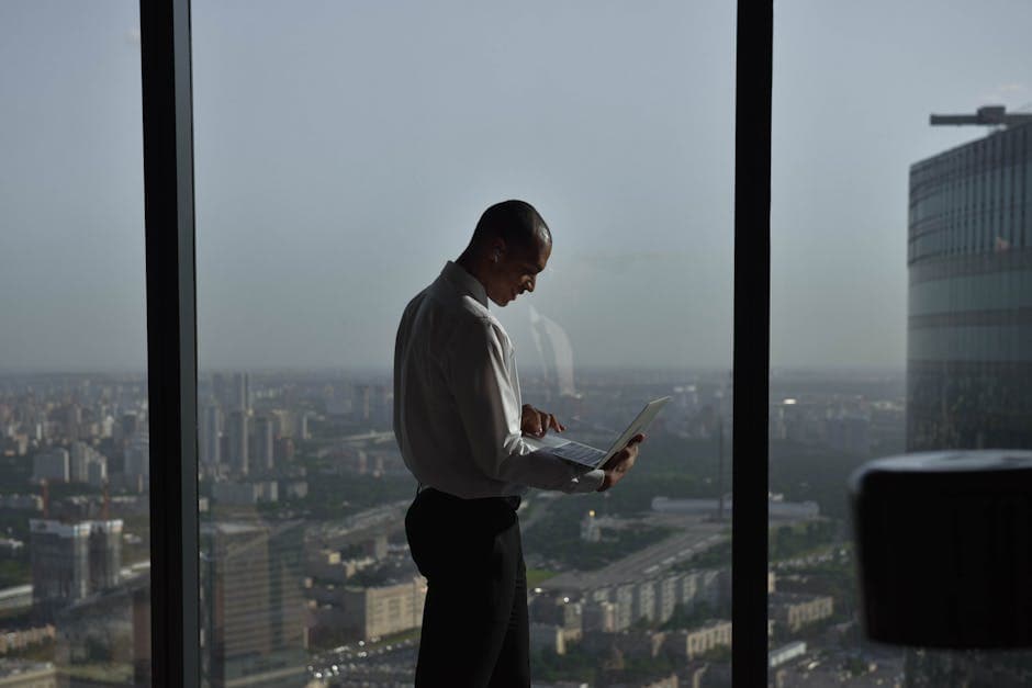 A man in a city skyscraper office using a laptop with a cityscape view.