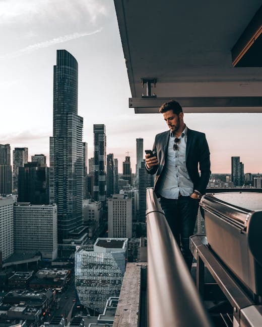 Man in black suit using phone on a Toronto rooftop with skyline view.
