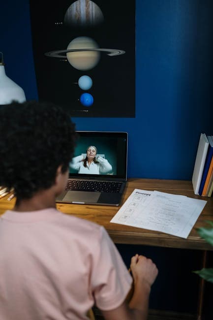 A child engaging in online learning at home with lesson papers and a laptop.