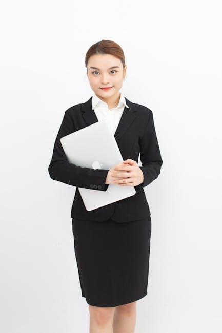 Confident woman in formal business attire holding a laptop, isolated on white background.