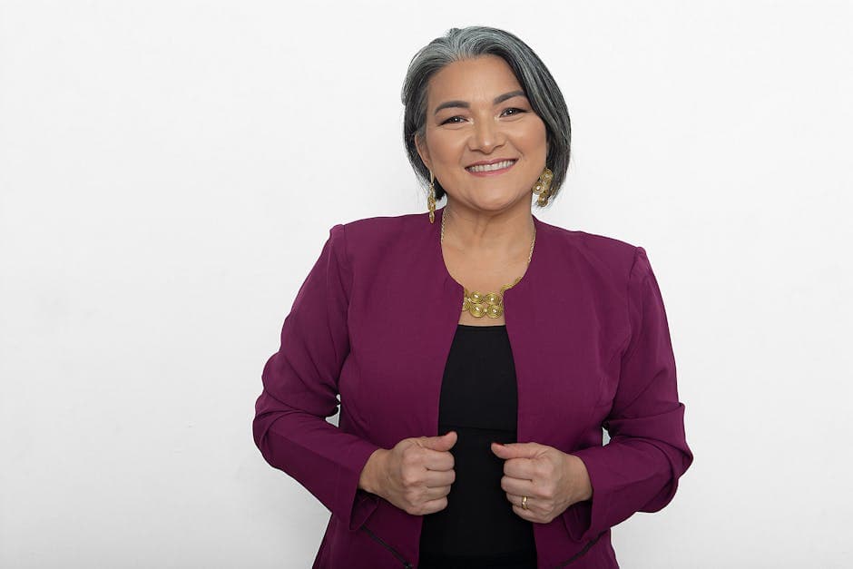 Confident woman with gray hair, wearing a purple blazer and smiling warmly.